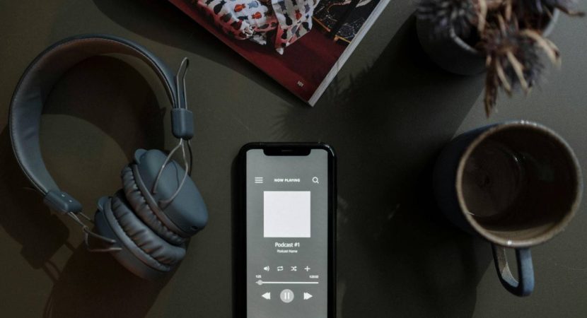 dark background with grey-ish headphones, a phone, and a cup